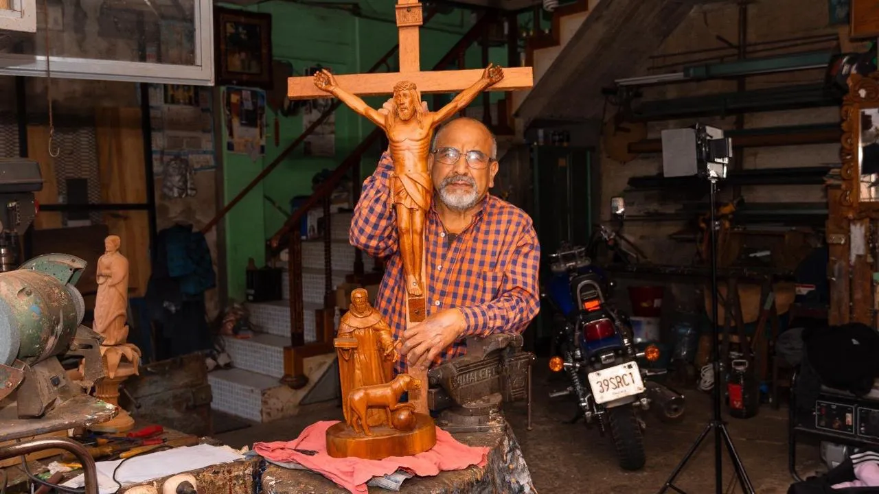 Artesano tallador de madera posando con un cristo en su taller